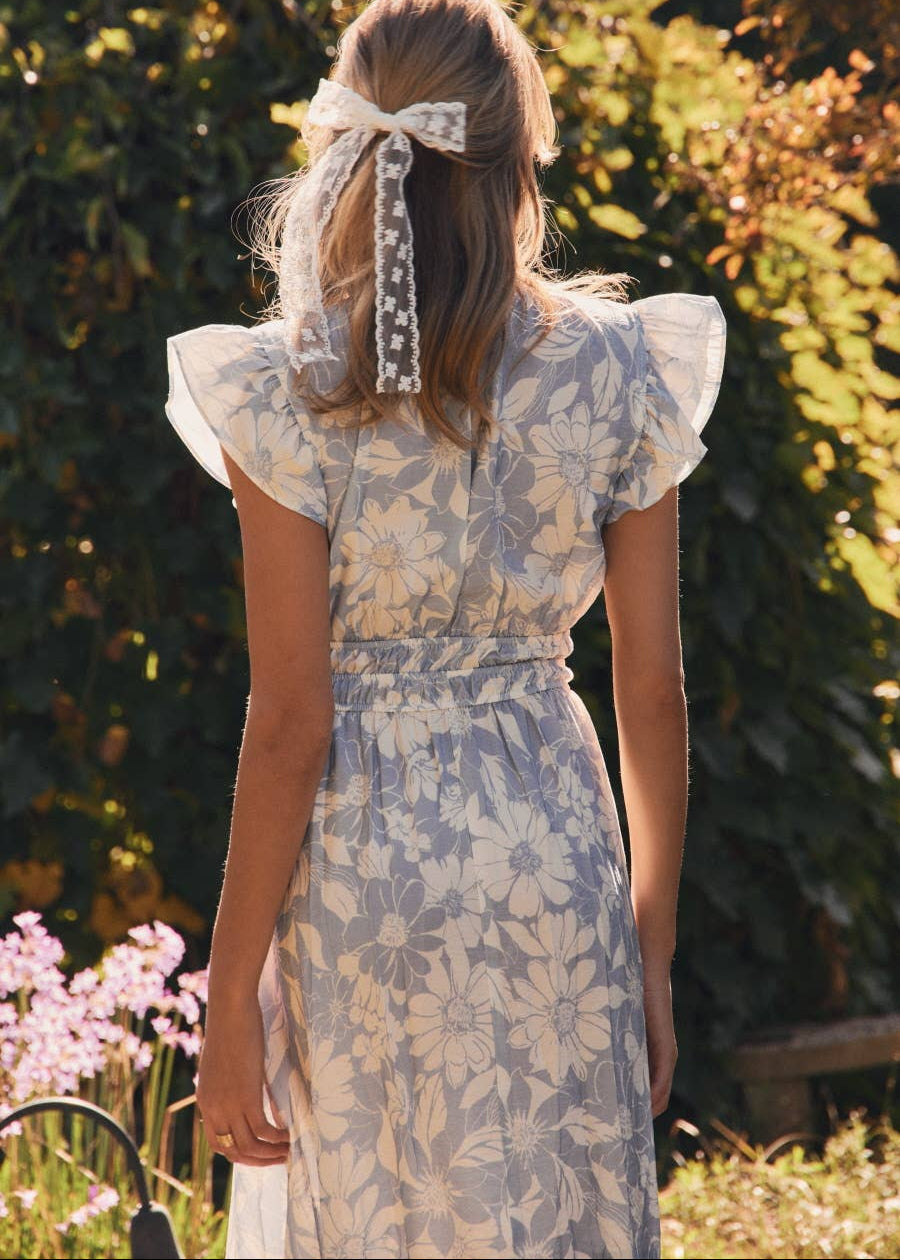 back view of women wearing floral print dress with flutter sleeves in a garden setting