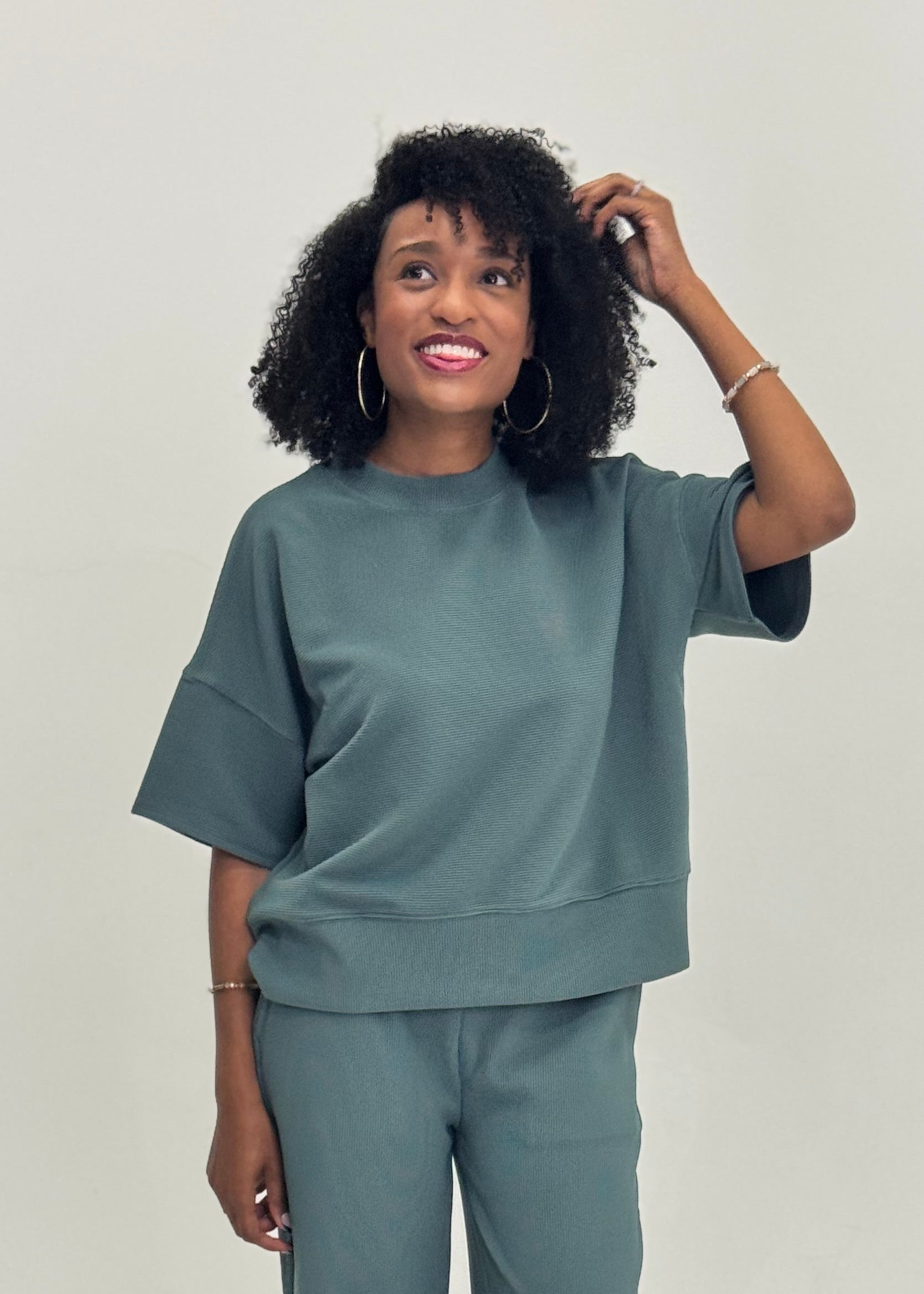 Woman wearing a sage green matching pant set on a plain background