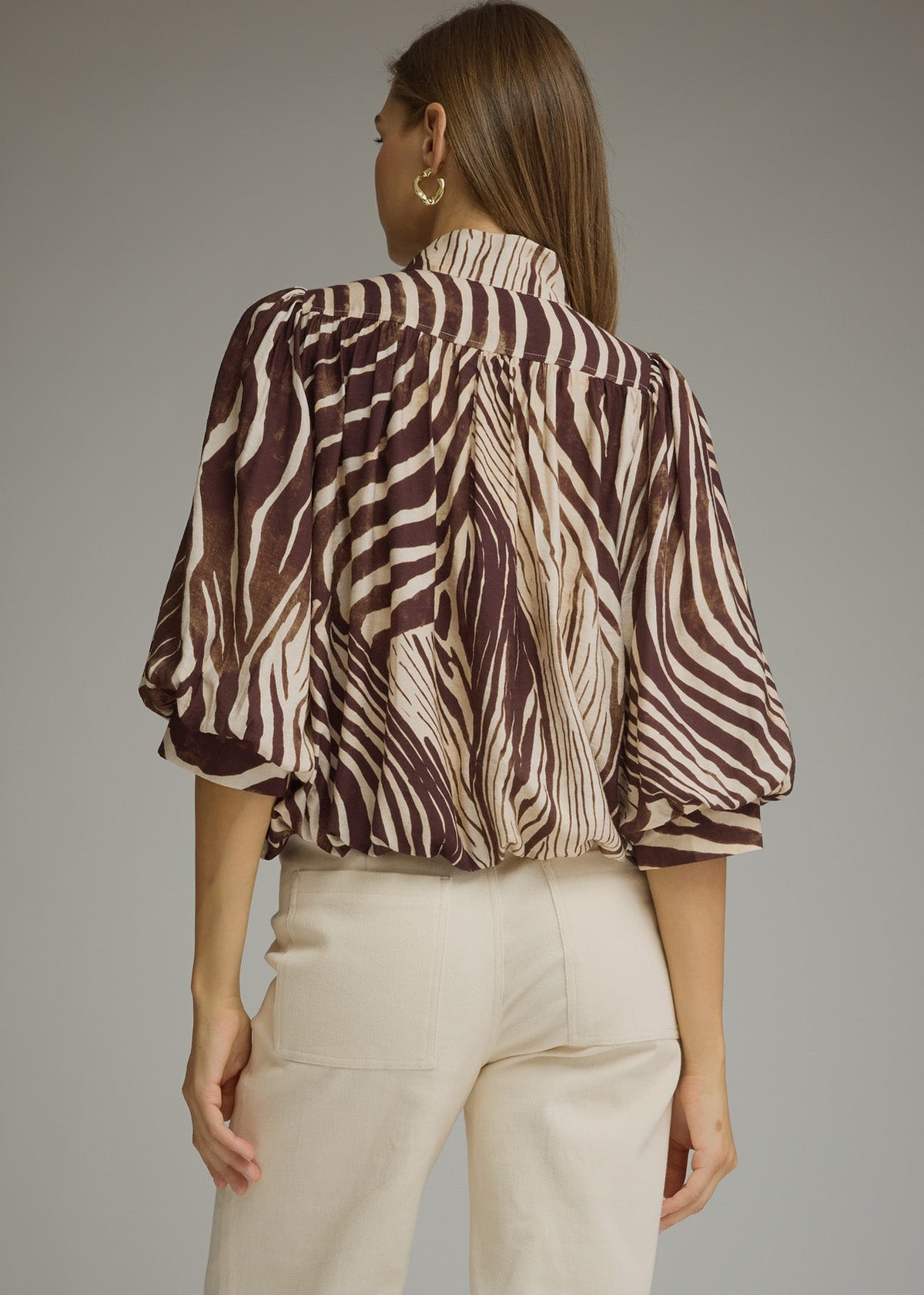 back view of women wearing zebra printed blouse with cuffed ballon sleeves and off white jeans