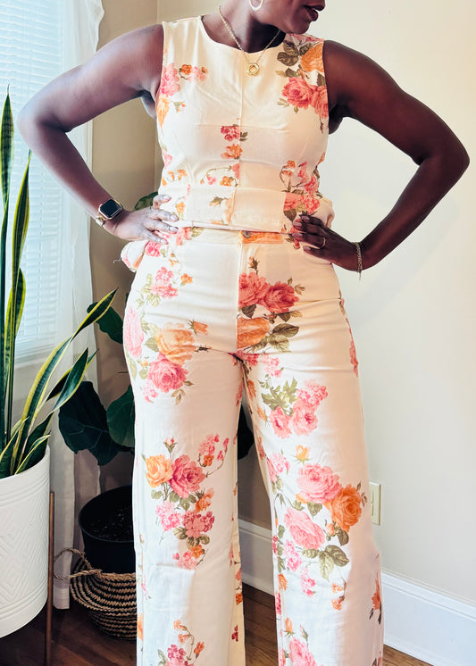 Woman wearing a floral pants matching standing in a room with plants and a window.