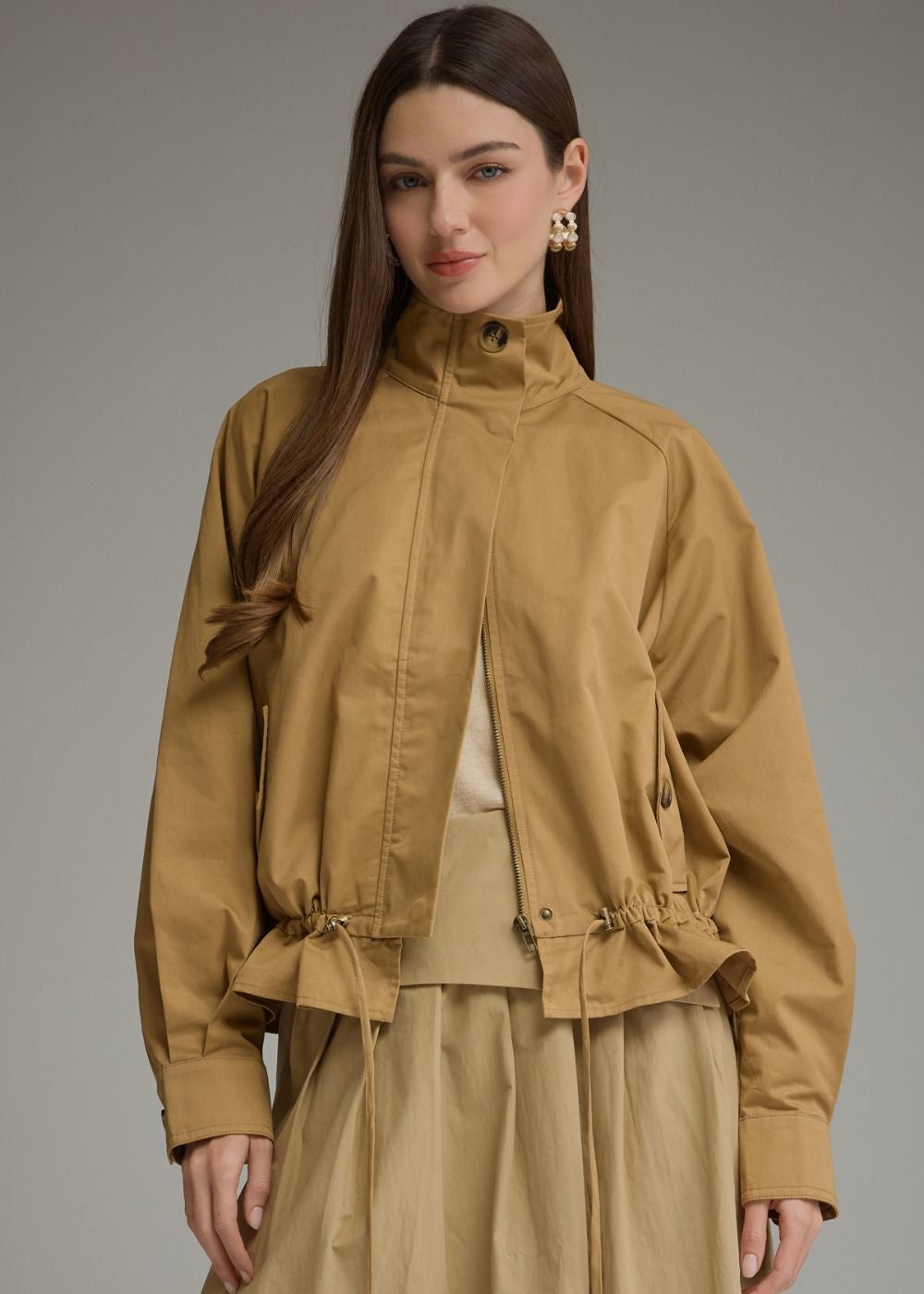 women wearing long sleeve tan jacket with drawstring waist and beige skirt and white undershirt