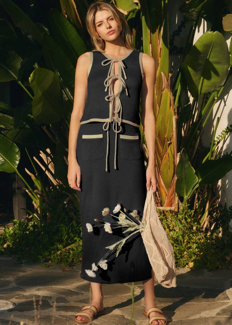women wearing a knit vest with open ties in black with beige trim with matching knit black skirt in mid length in tropical setting 