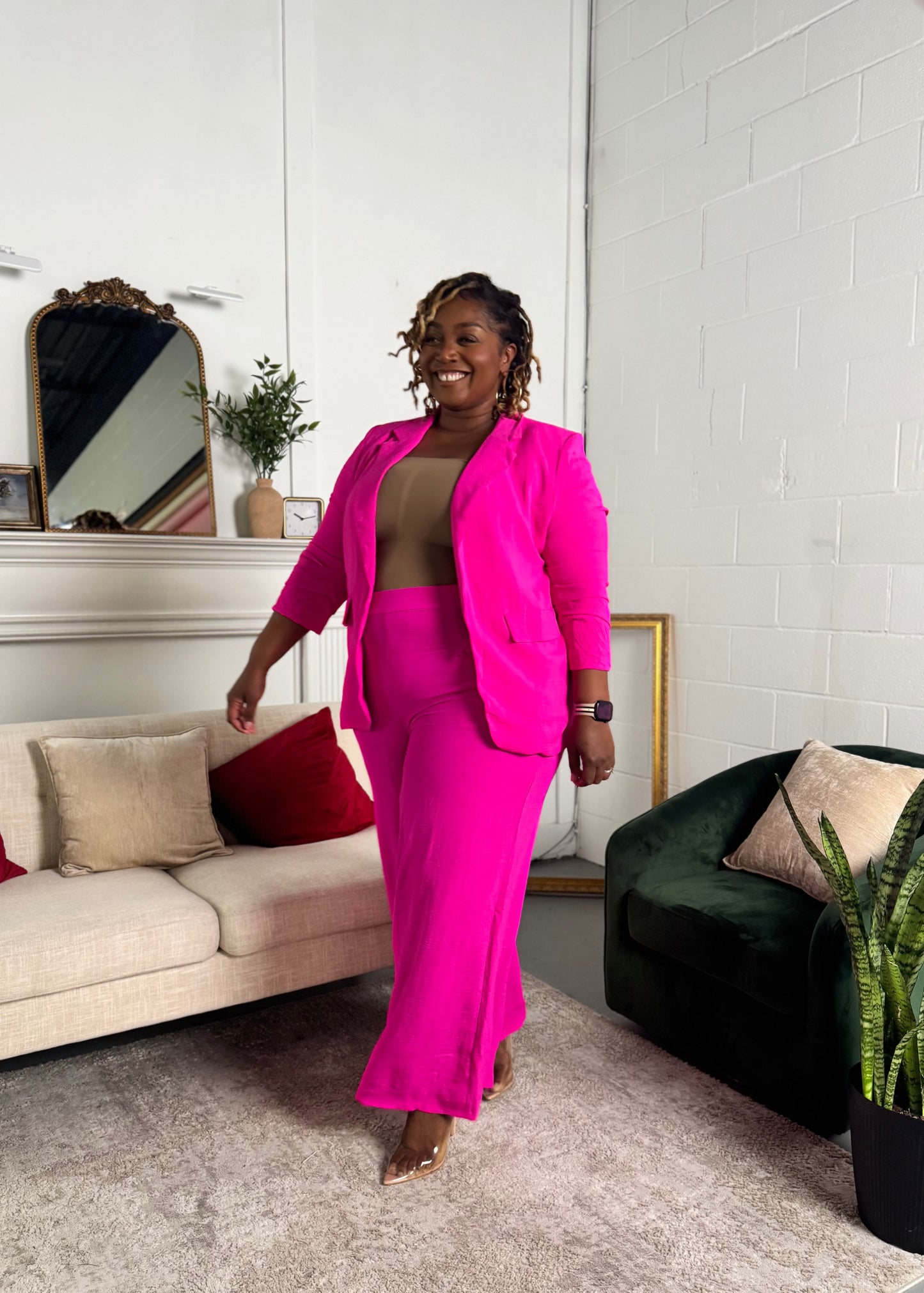 Plus size Woman in a bright pink pant suit standing in a living room.