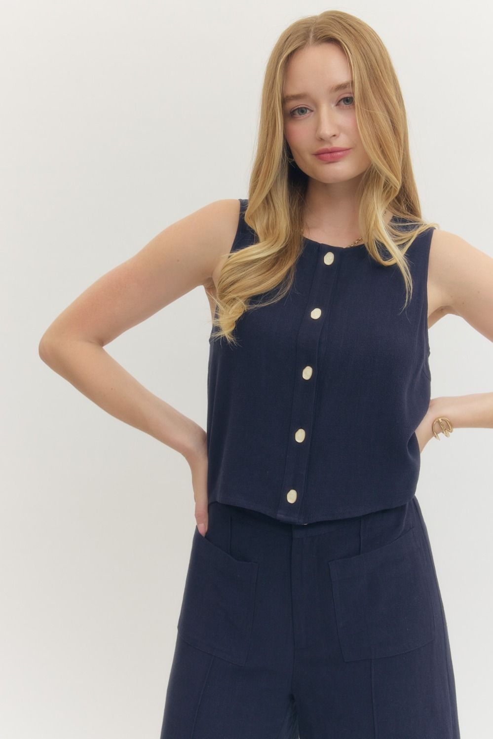 Woman wearing a navy sleeveless top with buttons and matching pants on a white background