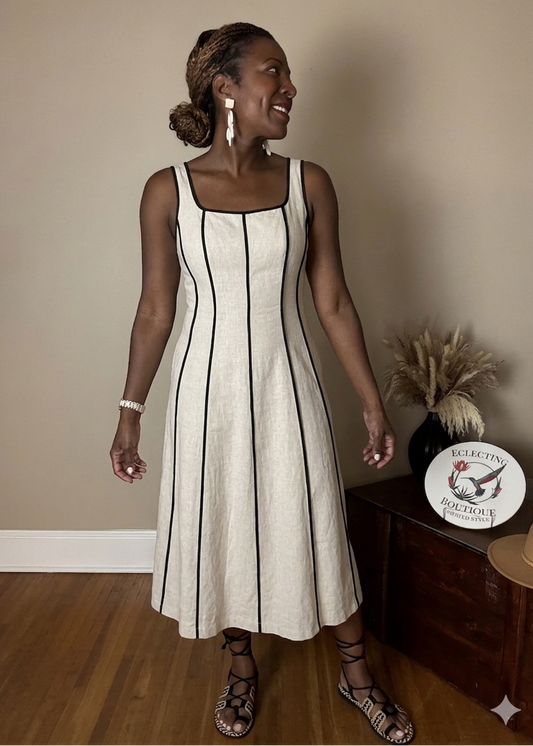 Woman wearing a linen dress with black piping standing indoors.